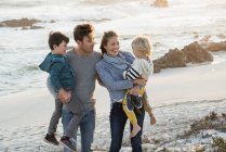 Familia feliz de pie en la playa al atardecer - foto de stock