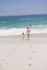 Pegadas na praia de areia com o homem correndo com o filho no fundo — Fotografia de Stock