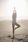 Junge schlanke Frau im Badeanzug praktiziert Yoga am Strand — Stockfoto