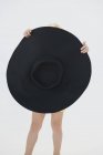 Menina escondendo atrás de grande chapéu preto no fundo branco — Fotografia de Stock