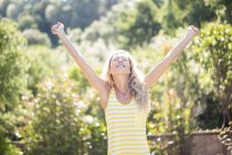 Happy woman with arms outstretched and eyes closed standing in garden — Stock Photo