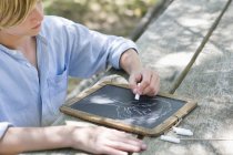 Хлопчик-підліток робить малюнок дерева на шифері на відкритому повітрі — стокове фото