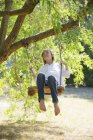 Щасливий босоніж хлопчик-підліток гойдається на дереві в літній сільській місцевості — стокове фото