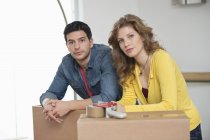 Пара наклоняющихся над картонными коробками в квартире и смотрящих в камеру — стоковое фото