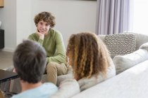 Улыбающийся мальчик разговаривает с родителями, сидя дома на диване в гостиной — стоковое фото