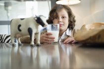 Retrato del niño sonriente sentado a la mesa con un vaso de leche - foto de stock