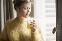Donna che beve tisana accanto alla finestra a casa — Foto stock