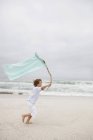 Menino correndo enquanto segurando bandeira na praia de areia — Fotografia de Stock