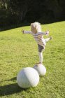 Fille équilibrage sur la sphère de pierre sur la pelouse verte — Photo de stock