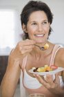 Усміхнена жінка їсть фруктовий салат і дивиться геть — стокове фото