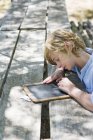 Adolescente escrevendo na ardósia à mesa de madeira ao ar livre — Fotografia de Stock