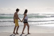 Juguetona joven pareja caminando en la playa juntos - foto de stock