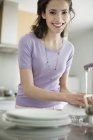 Mujer lavando platos en la cocina y mirando a la cámara - foto de stock