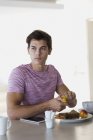 Вдумчивый молодой человек завтракает дома — стоковое фото