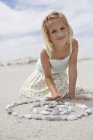 Portrait of little blonde girl playing with pebbles on beach — Stock Photo