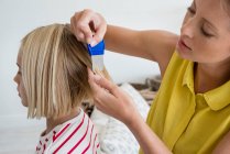 Madre usando peine de piojos en el cabello de su hija - foto de stock