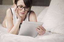 Жінка лежить на ліжку і використовуючи цифровий планшетний — стокове фото