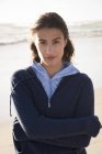Retrato de mulher com capuz em pé na praia com os braços cruzados — Fotografia de Stock