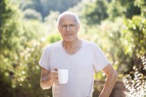 Ritratto di felice uomo anziano che si gode una tazza di caffè in giardino — Foto stock