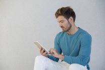 Young man using digital tablet against grey wall — Stock Photo