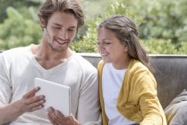 Счастливый отец с маленькой дочкой пользуются цифровым планшетом на качелях — стоковое фото