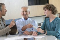 Smiling grandfather giving teenage grandson pocket money at table at home — Stock Photo