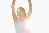 Glückliche junge Frau mit erhobenen Armen posiert am Strand im Sonnenlicht — Stockfoto