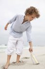 Хлопчик тягнеться за повідомлення в пляшку на піщаному пляжі — стокове фото