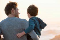 Happy father and son standing on the beach at sunset — Stock Photo