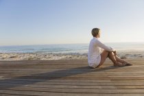 Розслаблена жінка сидить на прогулянці на березі моря і дивиться на погляд — стокове фото