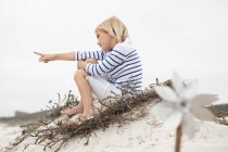 Rubia niña sentada en la arena y señalando en la distancia - foto de stock