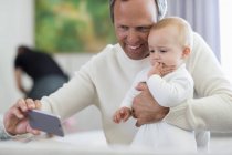 Щасливий батько з дочкою, яка бере селфі з телефоном вдома — стокове фото