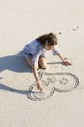 Sorrindo jovem mulher desenhando forma de coração na praia de areia — Fotografia de Stock