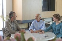 Щасливий старший чоловік з сином і онуком, сидить і розмовляє за столом у вітальні — стокове фото