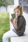 Retrato de menina loira sorridente segurando livro e sorrindo no alpendre ao ar livre — Fotografia de Stock