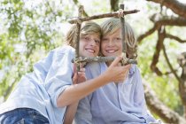 Портрет улыбающихся детей, смотрящих через раму из колючей древесины на открытом воздухе — стоковое фото