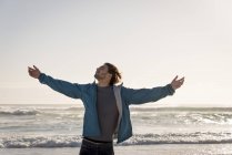 Jovem feliz com os braços estendidos em pé na praia — Fotografia de Stock