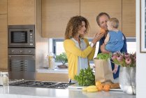 Woman giving orange to baby daughter in father hands in kitchen — Stock Photo