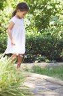 Bambina in bianco abito estivo passeggiando nel giardino soleggiato — Foto stock