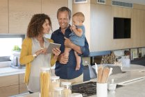 Casal usando tablet digital com filha bebê na cozinha — Fotografia de Stock
