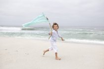 Niño corriendo mientras sostiene la bandera en la playa de arena - foto de stock