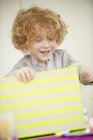Усміхнений хлопчик з світлим волоссям відкриває подарунок на день народження — стокове фото