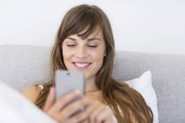 Joyeux message de jeune femme avec téléphone portable au lit — Photo de stock