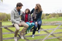Junge sitzt mit Eltern auf Holzzaun im Grünen — Stockfoto