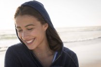 Close-up de jovem mulher sorridente com capuz jaqueta na praia — Fotografia de Stock