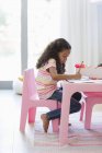 Маленькая девочка делает домашнее задание за розовым столом в комнате — стоковое фото