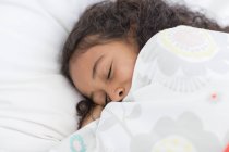 Крупным планом улыбающейся маленькой девочки, спящей на кровати — стоковое фото