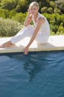Dreamy relaxed woman sitting at poolside and looking at water — Stock Photo