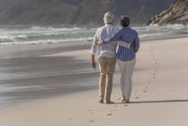 Вид сзади на босоногую старшую пару, идущую по песчаному пляжу — стоковое фото