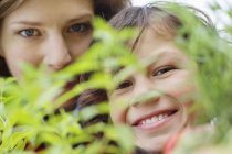 Ritratto di ragazzo sorridente con madre che guarda oltre la pianta — Foto stock